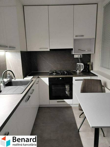 Konyha fehér szekrényekkel és asztallal egy kétszobás lakásban, fa dekoros padlóval.