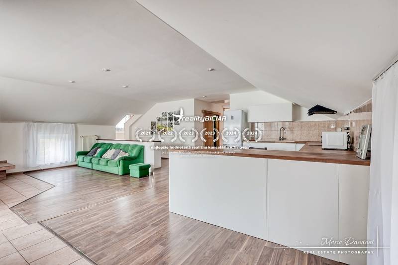 Nappali konyhával, zöld kanapé, fehér bútor, fa dekoros padló.