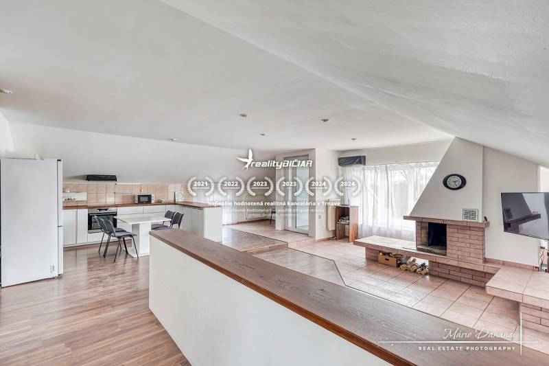 Nappali kandallóval és konyhai résszel, fa dekoros padlóval, világos szoba.