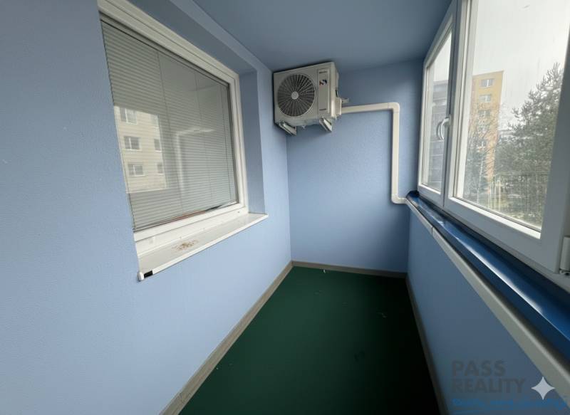 Üvegezett lodzsa klímaberendezéssel egy 2 szobás lakásban, redőnyökkel és zöld szőnyeggel felszerelve.