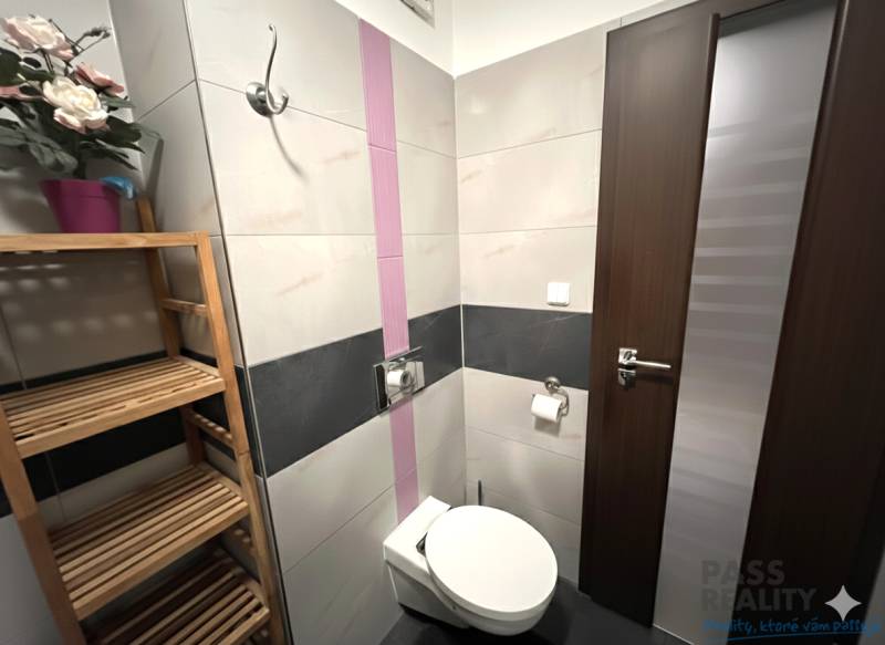 Fürdőszoba egy kétszobás lakásban WC-vel, fa polccal és dekoratív virágokkal.