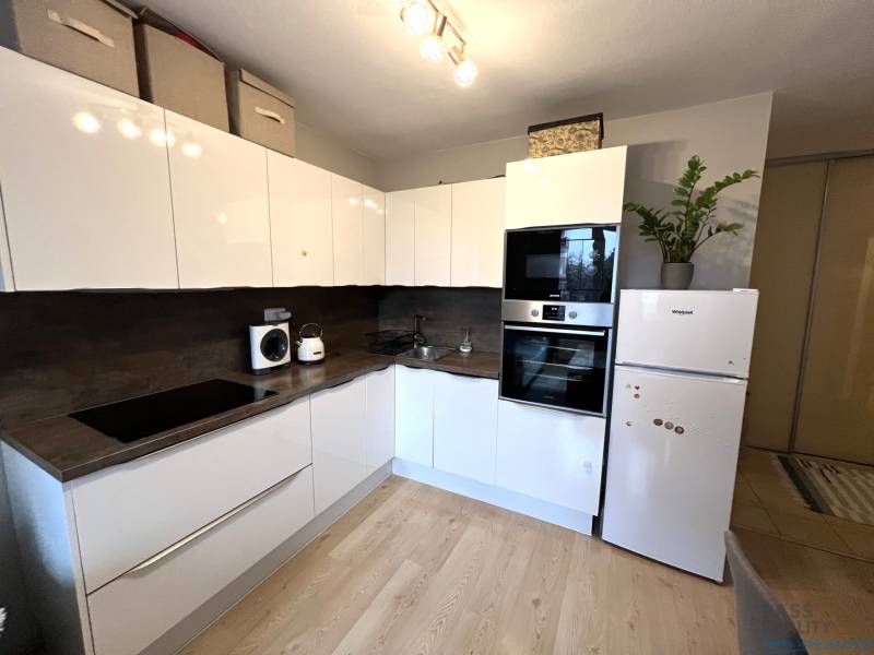 Konyha egy kétszobás lakásban fehér szekrényekkel, készülékekkel és fa mintázatú padlóval.