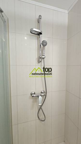 Zuhanykabin egy garzonlakásban fehér csempékkel és krómozott zuhanycsapteleppel.