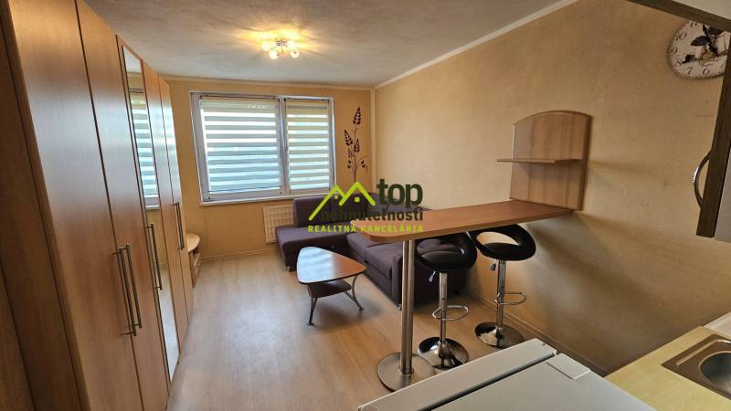 Garzonlakás fa mintázatú padlóval, konyhapulttal és kanapéval.