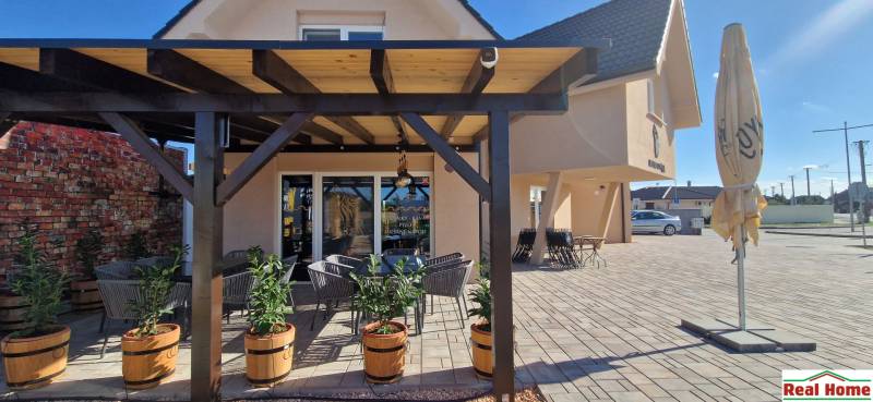 Újfalusi vendéglátóhely pergolával, virágládákkal és kültéri ülőhellyel a burkolaton.