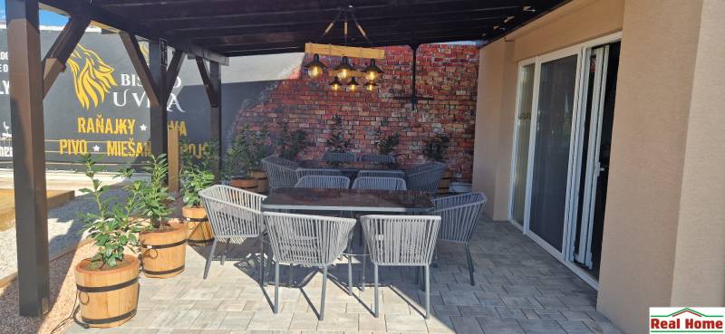 Új Dedinán található kültéri vendéglátóhelyeken rattan székek és téglafal van.