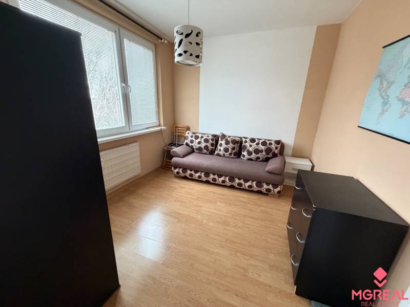 Szoba kanapéval, komóddal és fa dekorációjú padlóval egy háromszobás lakásban.