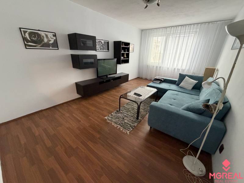 Nappali fa hatású padlóval és kanapéval egy háromszobás lakásban.