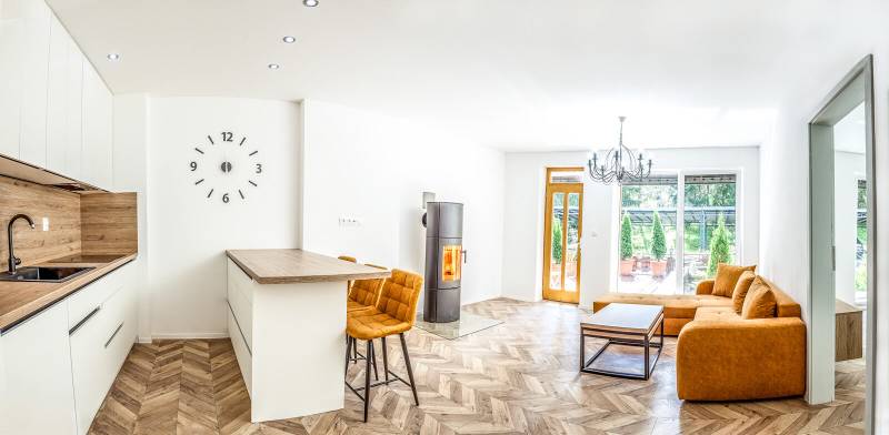 Világos nyaraló apartman konyhával, narancssárga kanapéval és fa mintázatú padlóval.