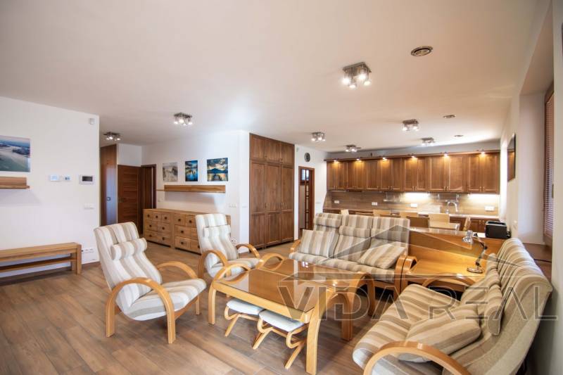 Családi ház belső tere tágas nappalival, konyhabútorral és fa mintázatú padlóval.