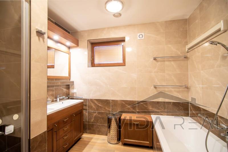 Fürdőszoba családi házban káddal, mosdóval, zuhanyzóval és fa dekoros padlóval.