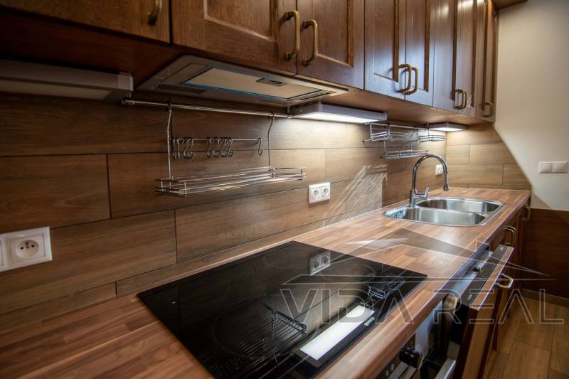 Családi ház konyhája fa dekoros padlóval és fából készült konyhabútorral.