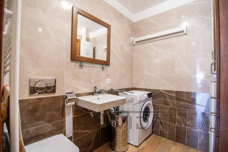 Fürdőszoba családi házban mosógéppel, mosdóval és fa mintázatú padlóval.