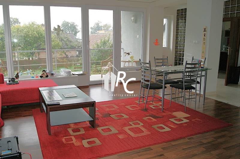 Nappali egy családi házban, fa mintázatú padlóval és piros szőnyeggel.