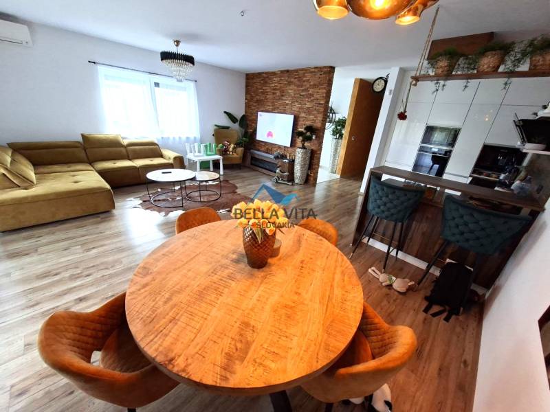 Nappali egy családi házban kanapéval, étkezőasztallal és fa mintázatú padlóval.