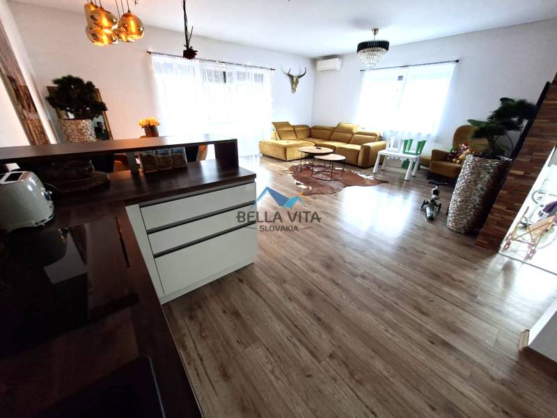 Nappali egy családi házban, fa mintázatú padlóval és világos kanapéval.