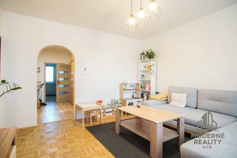 Nappali egy háromszobás lakásban, fa dekoros padlóval és világos bútorokkal.