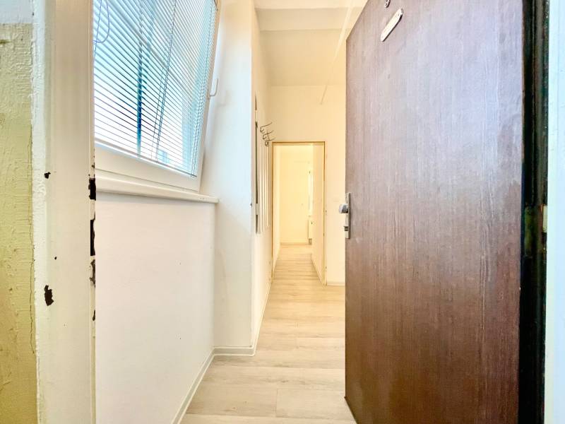 Folyosó fa hatású padlóval, fehér falakkal, nagy ablakkal és redőnyökkel.