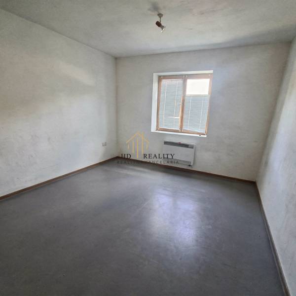 Fehér falú, szürke padlójú és kis ablakú szoba a gyártóhelyiségben.