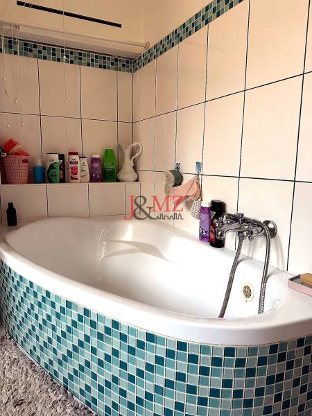 Fürdőszoba sarokkáddal és kék-fehér csempével egy kétszobás lakásban.