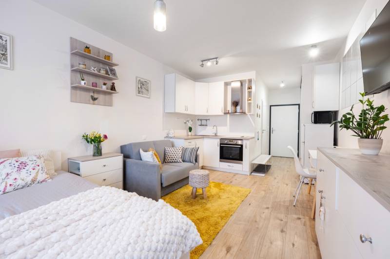 Világos belső tér egy egyszobás lakásban konyhával, ággyal és fa dekorációjú padlóval.