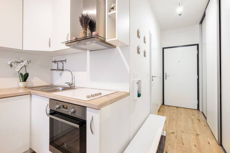 Világos konyha fa dekorációval az egyszobás lakásban, bejárati folyosó.