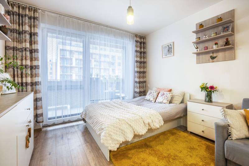 Világos egyszobás lakás ággyal, szőnyeggel és fa dekor padlóval.