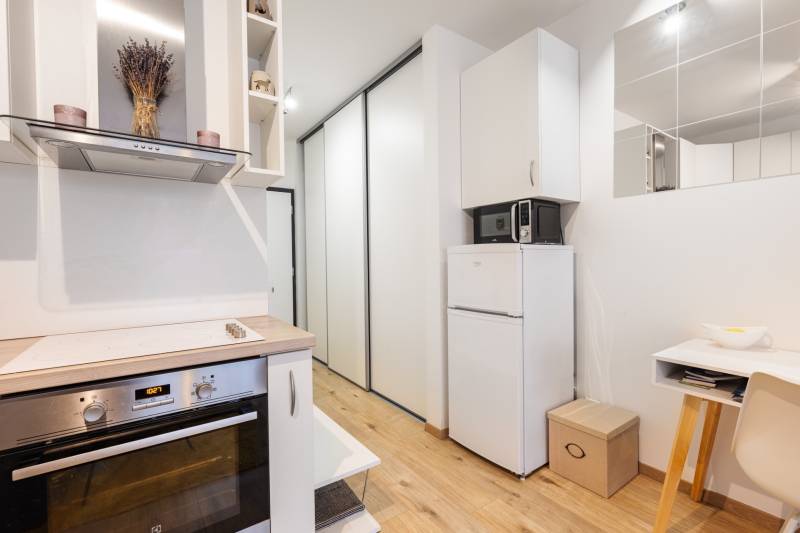 Kompakt konyha főzőlappal, hűtőszekrénnyel és fa dekor padlóval egy egyszobás lakásban.