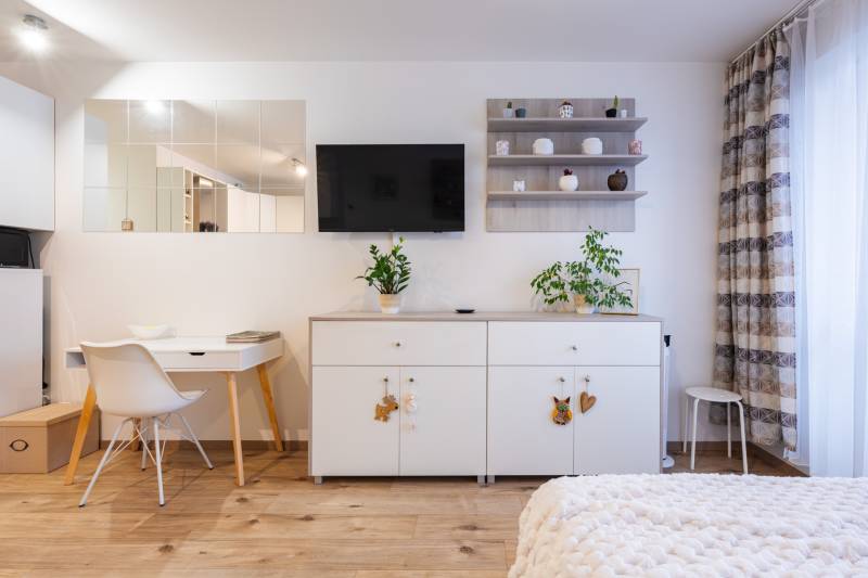 1 szobás lakás belső tere fehér bútorokkal és fa dekorációjú padlóval.