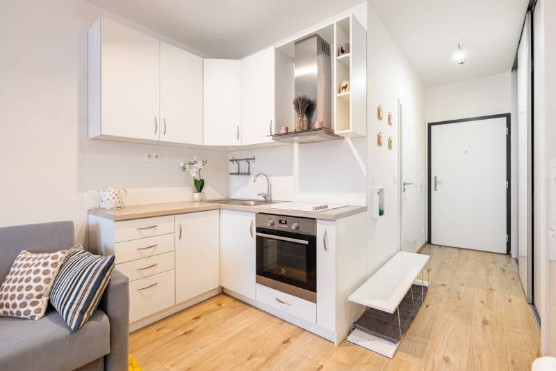 Konyha fehér szekrényekkel egy egyszobás lakásban és fa mintázatú padlóval.