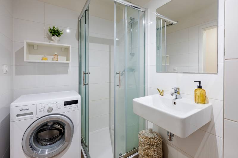 Fürdőszoba mosógéppel, zuhanyzóval és mosdóval egy egyszobás lakásban.