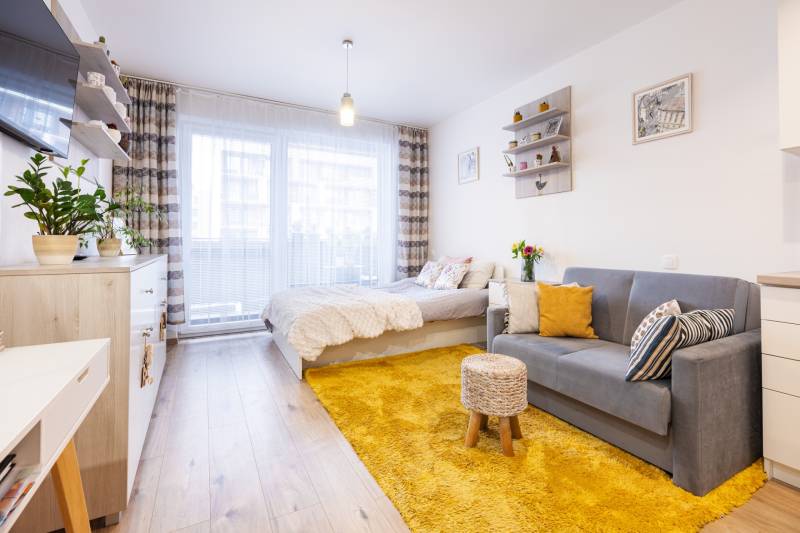 Egyszobás lakás fa dekor padlóval, ággyal, kanapéval és sárga szőnyeggel.