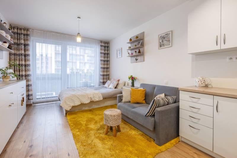 Világos 1 szobás lakás kanapéval, ággyal és fa dekorációjú padlóval.