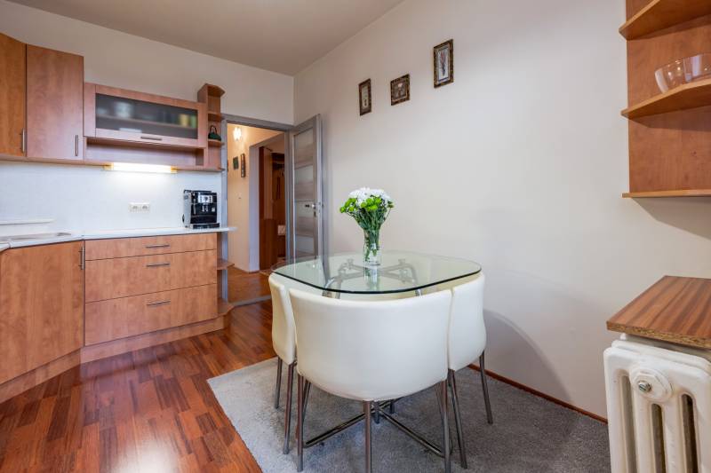 Konyha egy 4 szobás lakásban üvegasztallal, fa dekoros padló, fehér falak.