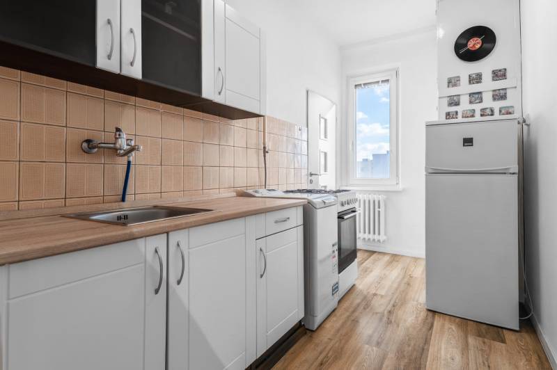 Kuchyňa v 1-izbovom byte s podlahou s dreveným dekorom a bielymi skrinkami.