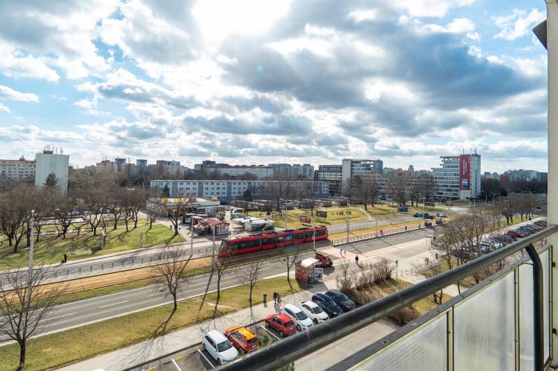 Výhľad na rušnú ulicu v Bratislave - Ružinov, Súmračná, s električkou a parkom.