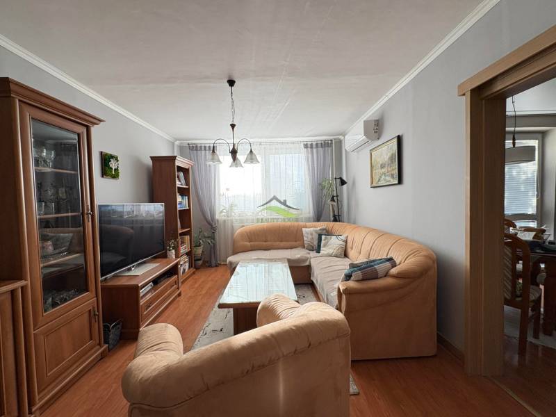 Nappali kényelmes kanapéval, fa dekorációjú padlóval és kellemes világítással egy háromszobás lakásban.