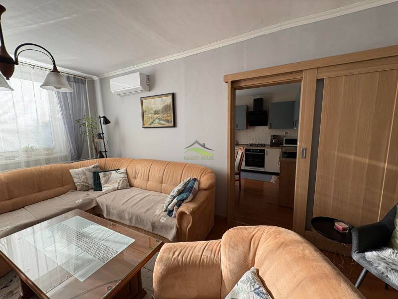 Nappali kanapéval, üvegasztallal és konyhával egy háromszobás lakásban.