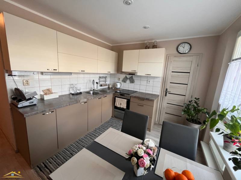 Konyha egy háromszobás lakásban világos szekrényekkel és étkezőasztallal.