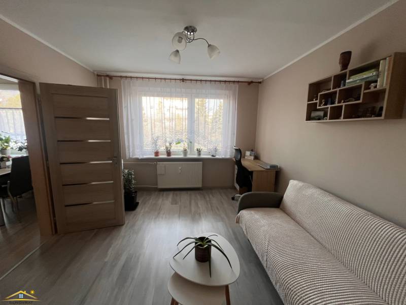 Nappali egy háromszobás lakásban fa mintázatú padlóval, kanapéval és asztallal.