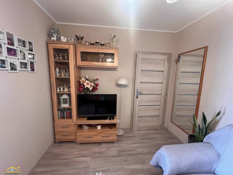 Szoba televízióval, tükörrel, fa bútorzattal és kanapéval, egy háromszobás lakásban.