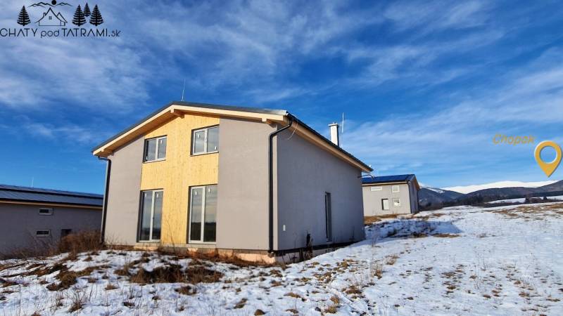 Ház Dolná Lehota-ban fa burkolattal, havas táj és hegyek a láthatáron.