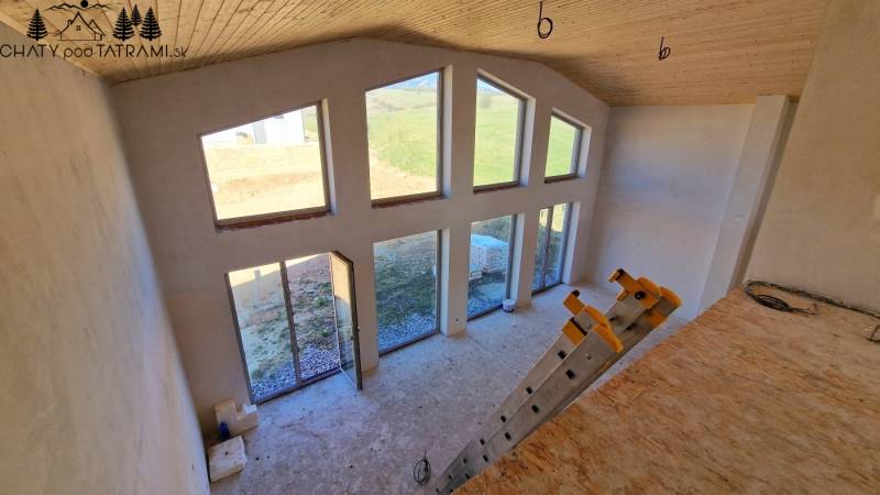 Egy kunyhó belseje nagy ablakokkal, lépcsőkkel és fa dekorációjú padlóval.