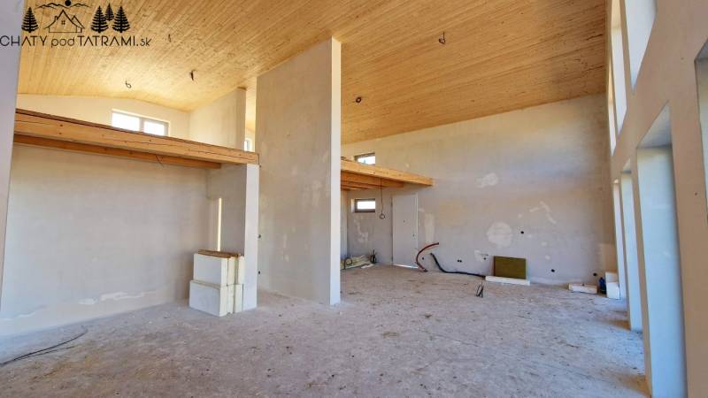 Egy magas mennyezetű házikó belseje, nyersen kialakított falak és finom fa dekorációk.