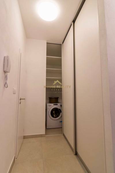 Egy szűk folyosó egy egyszobás lakásban mosógéppel és tolóajtókkal.