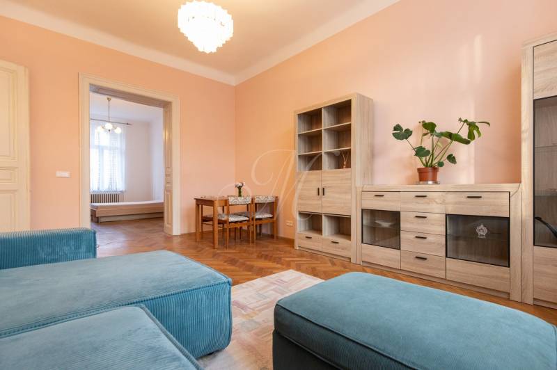 Nappali egy háromszobás lakásban, fa dekorációjú padlóval és pasztell színű falakkal.