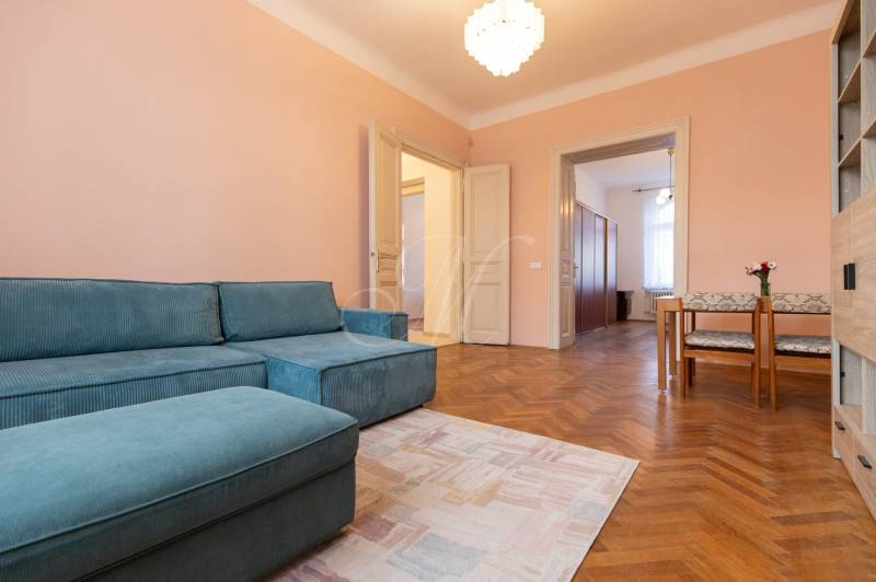 Szoba egy háromszobás lakásban kék kanapéval, fa dekorációjú padlóval és étkező sarokkal.