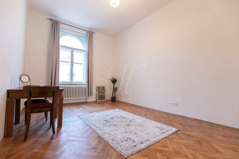 Szoba egy háromszobás lakásban, fa dekorációjú padlóval, szőnyeggel és asztallal.