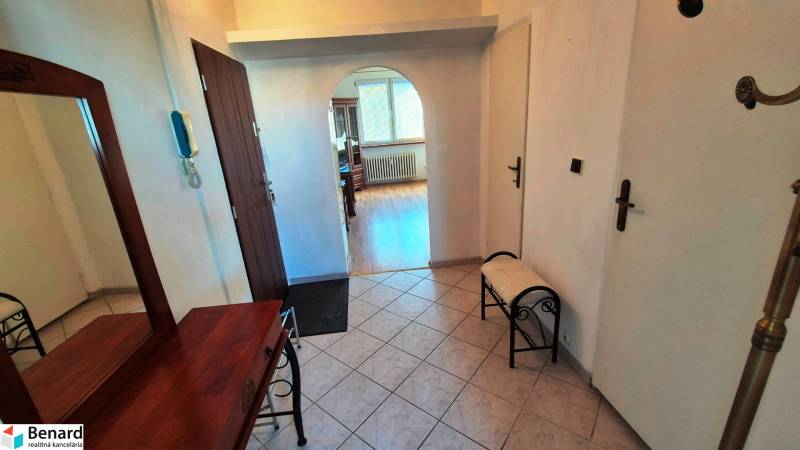 Folyosó íves átjáróval egy kétszobás lakásban, fa dekorációjú padló, tükör, pad.