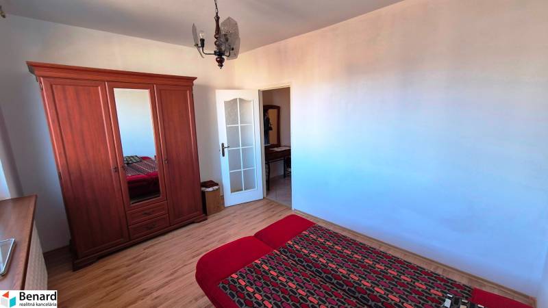 Hálószoba egy kétszobás lakásban fa hatású padlóval, szekrénnyel és ággyal.